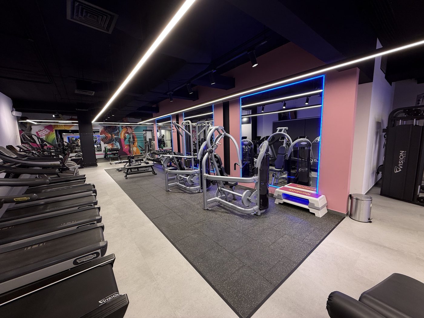 Treadmills and strength machines in front of mirrors and a pink feature wall